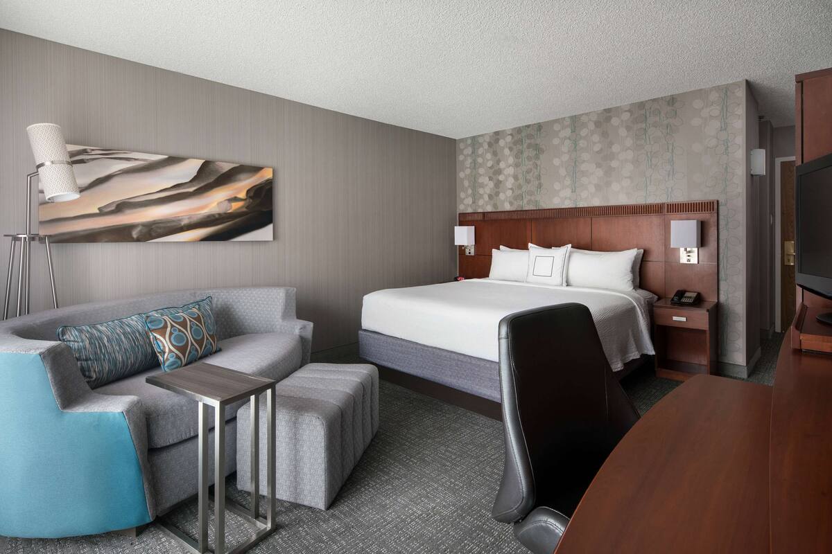 A hotel room with a bed, a sofa, a desk, and a TV.