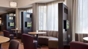 A modern hotel lobby with seating areas, a fireplace, and large windows with curtains.