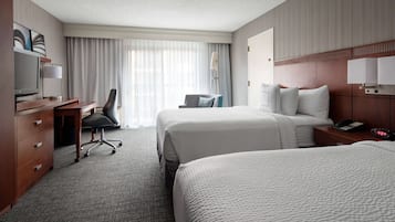 A hotel room with two beds, a desk with a chair, a TV, and a lamp.