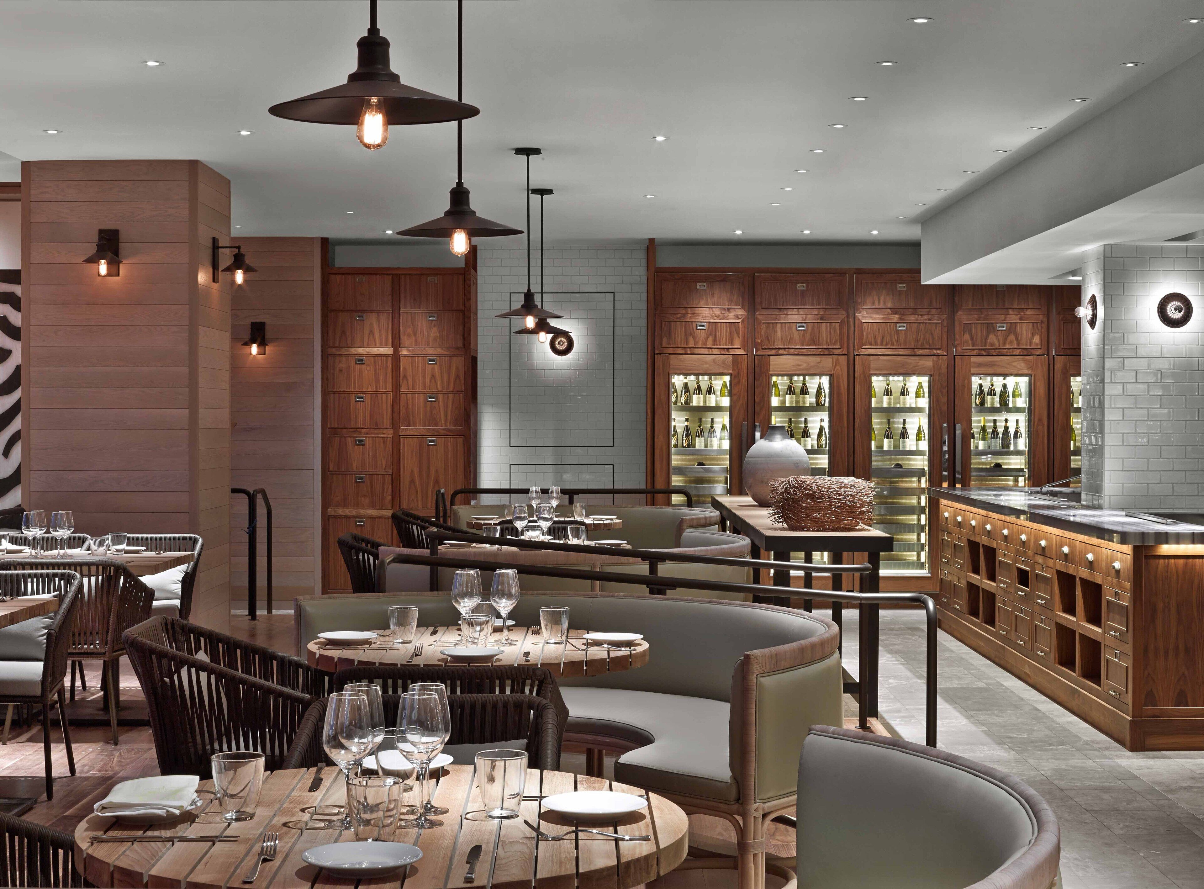 Un interior de restaurante moderno con mobiliario de madera, iluminación colgante y una vitrina de vinos.