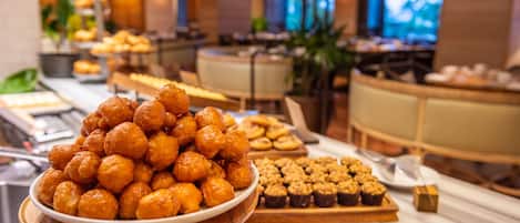 Un buffet proposant une variété de viennoiseries et de desserts, avec, au premier plan, un grand saladier rempli de petits gâteaux ronds.