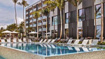 A modern hotel with a pool area, lounge chairs, and palm trees.