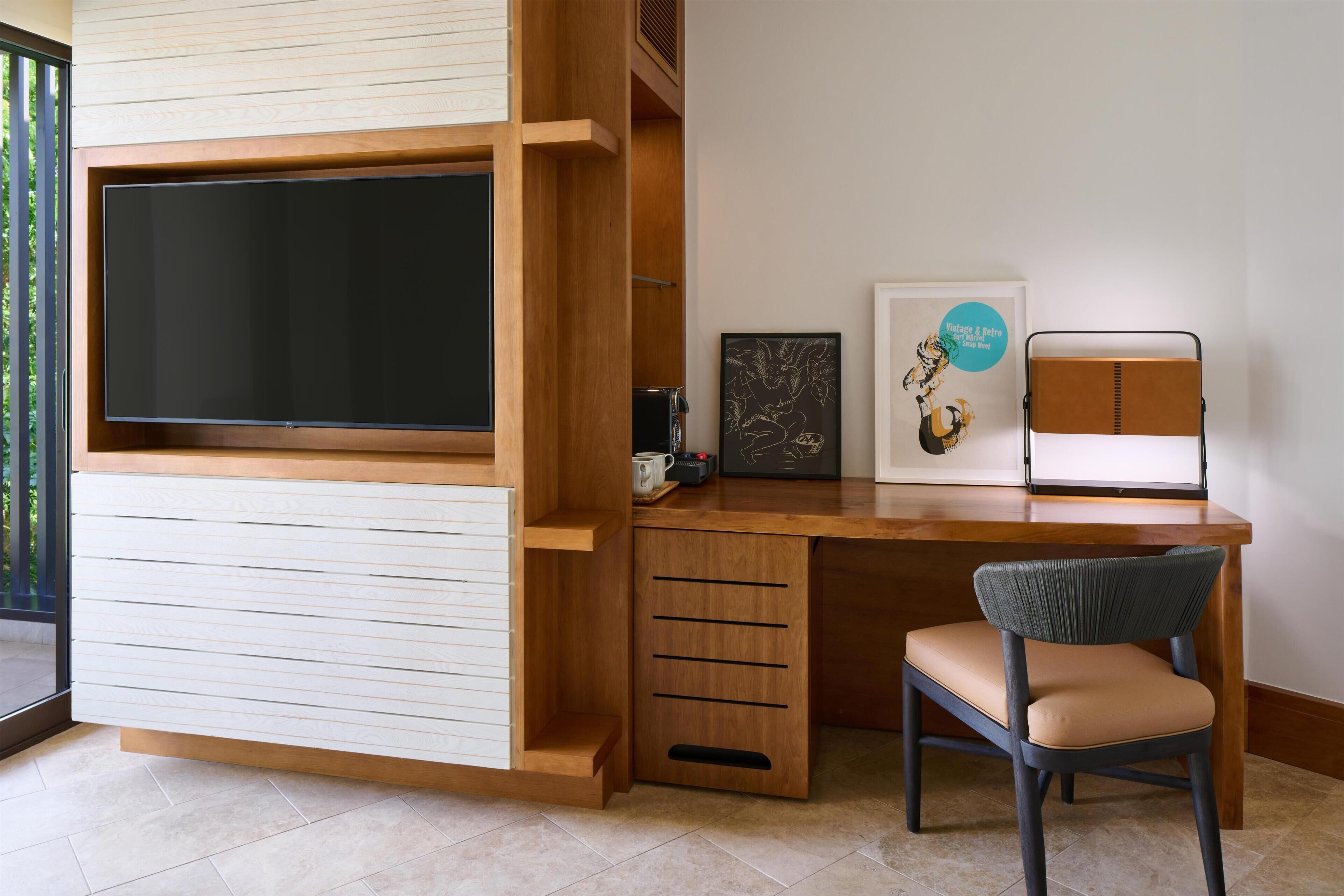 A modern room with a built-in TV, a wooden desk, a chair, and a framed picture on the wall.
