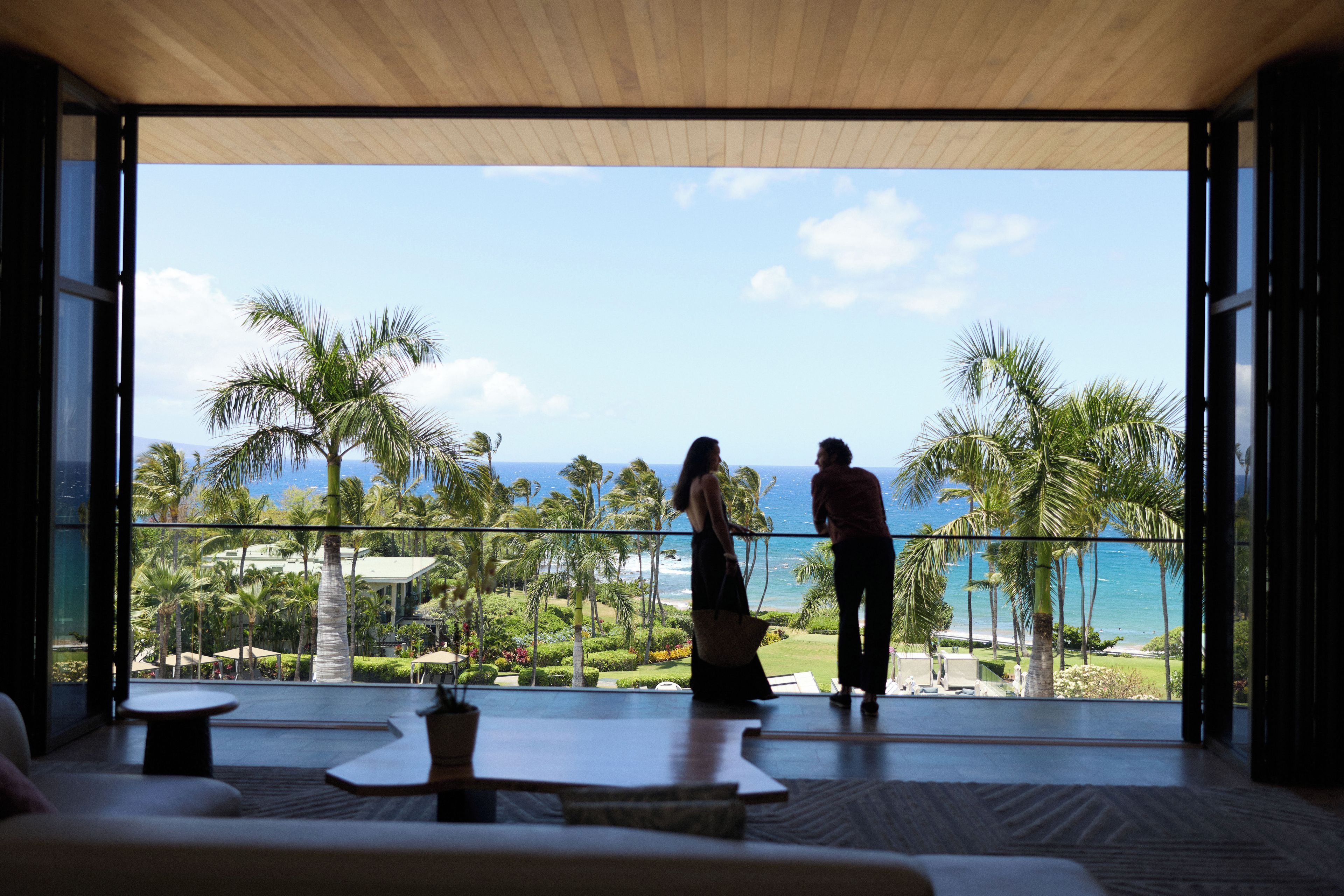 Une pièce dotée d’une grande porte vitrée donnant sur un balcon qui offre une vue imprenable sur un paysage tropical, avec des palmiers et l’océan à l’horizon.
