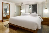 A hotel room with a large bed, a mirror, and a window with blinds.