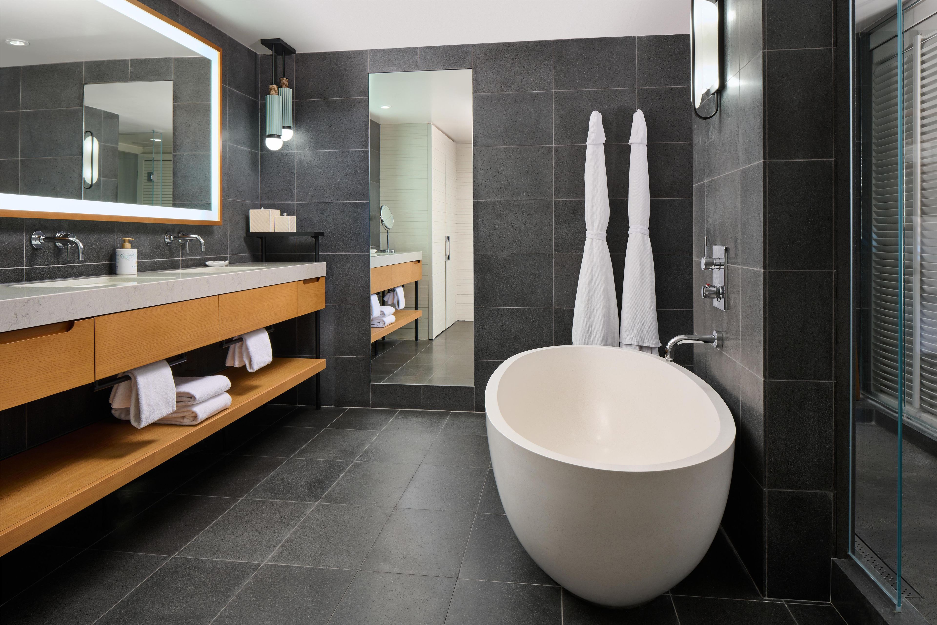 A modern bathroom with a large freestanding bathtub, a wooden vanity with a mirror, and a glass shower enclosure.