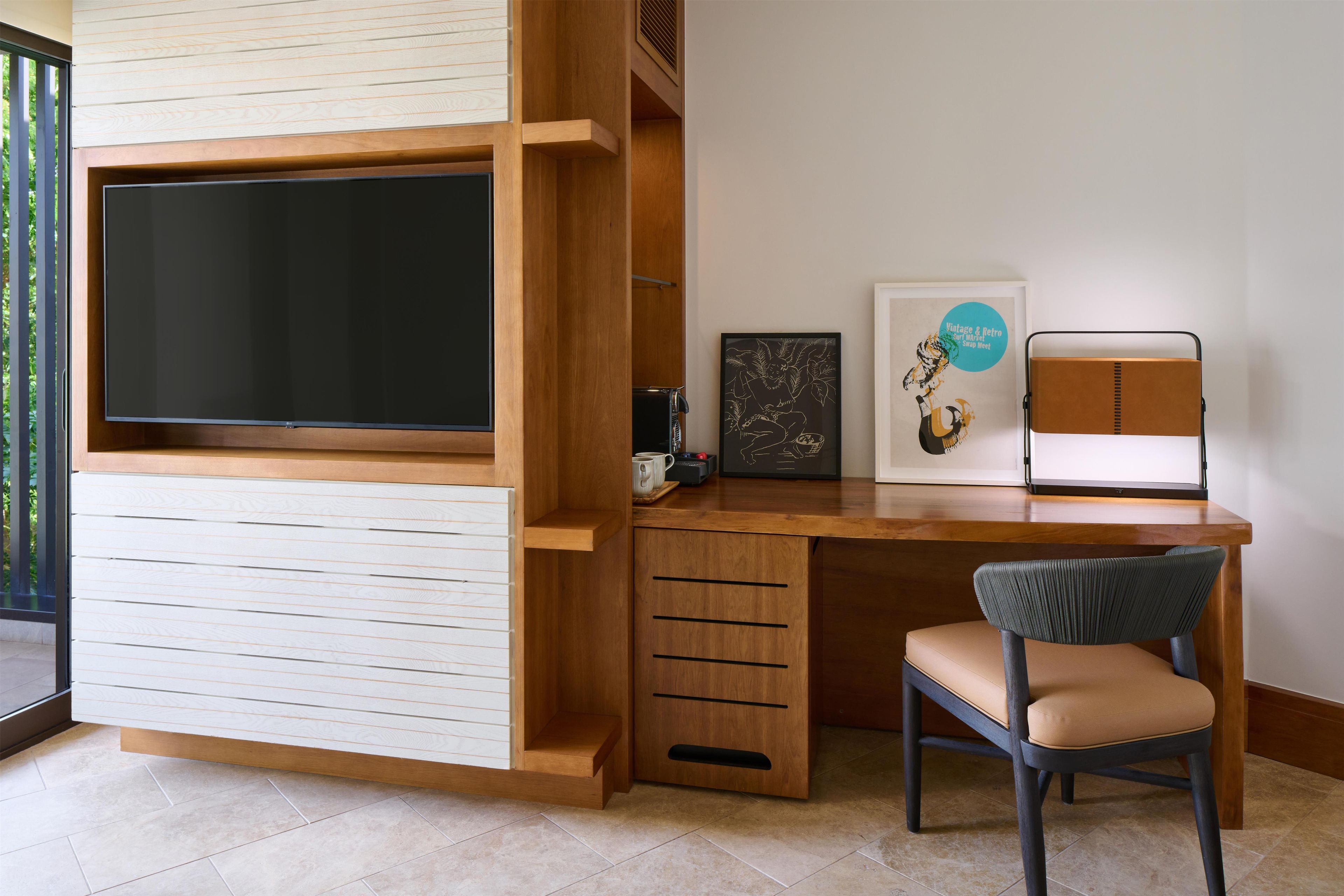 Une chambre moderne équipée d’un téléviseur encastré, d’un bureau, d’une chaise et d’une œuvre d’art encadrée au mur.