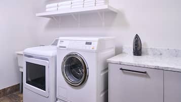 A laundry area with a front-loading washing machine, a dryer, and an iron on a marble countertop.