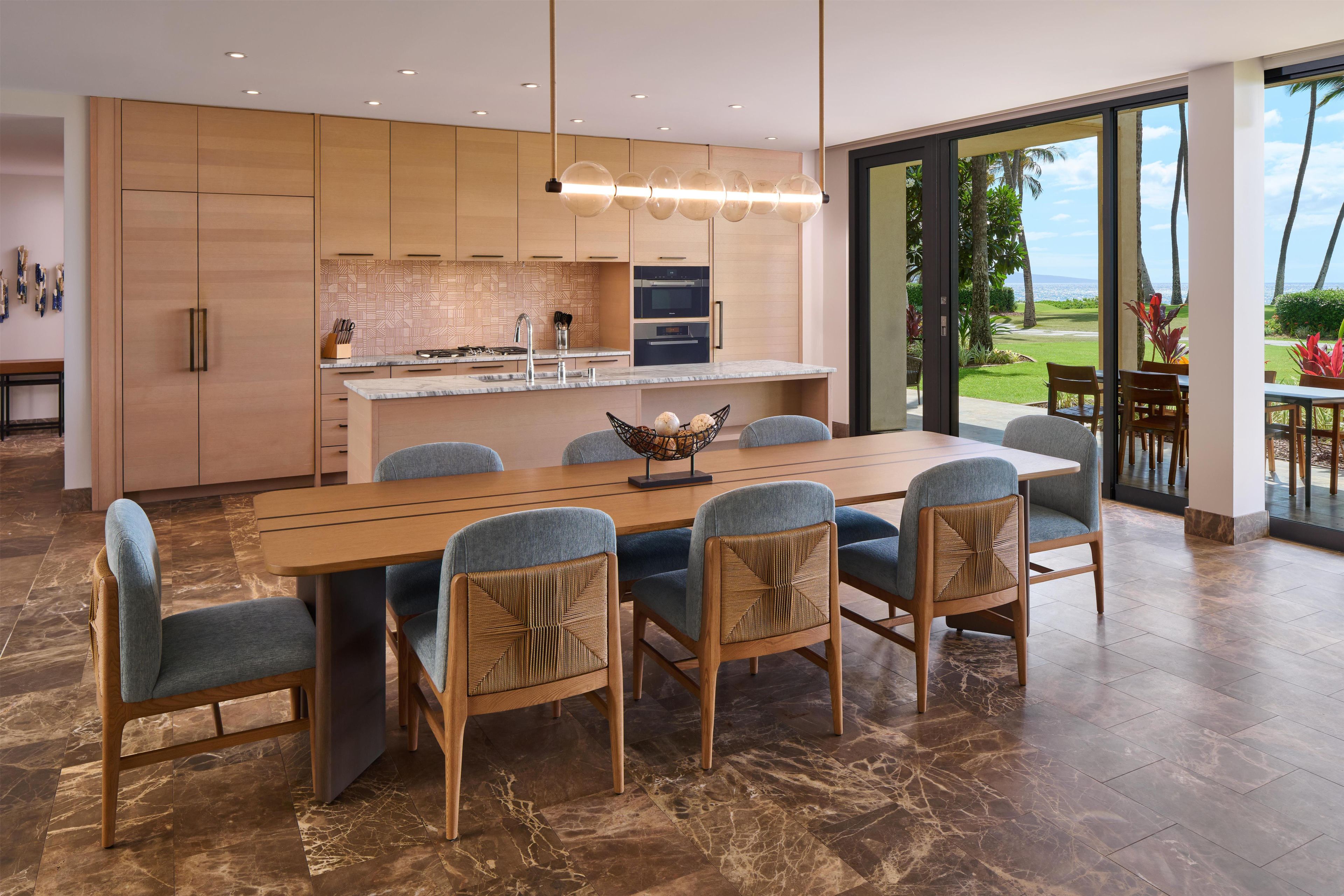 A modern kitchen with a large island, wooden cabinets, and a view of the outdoors.