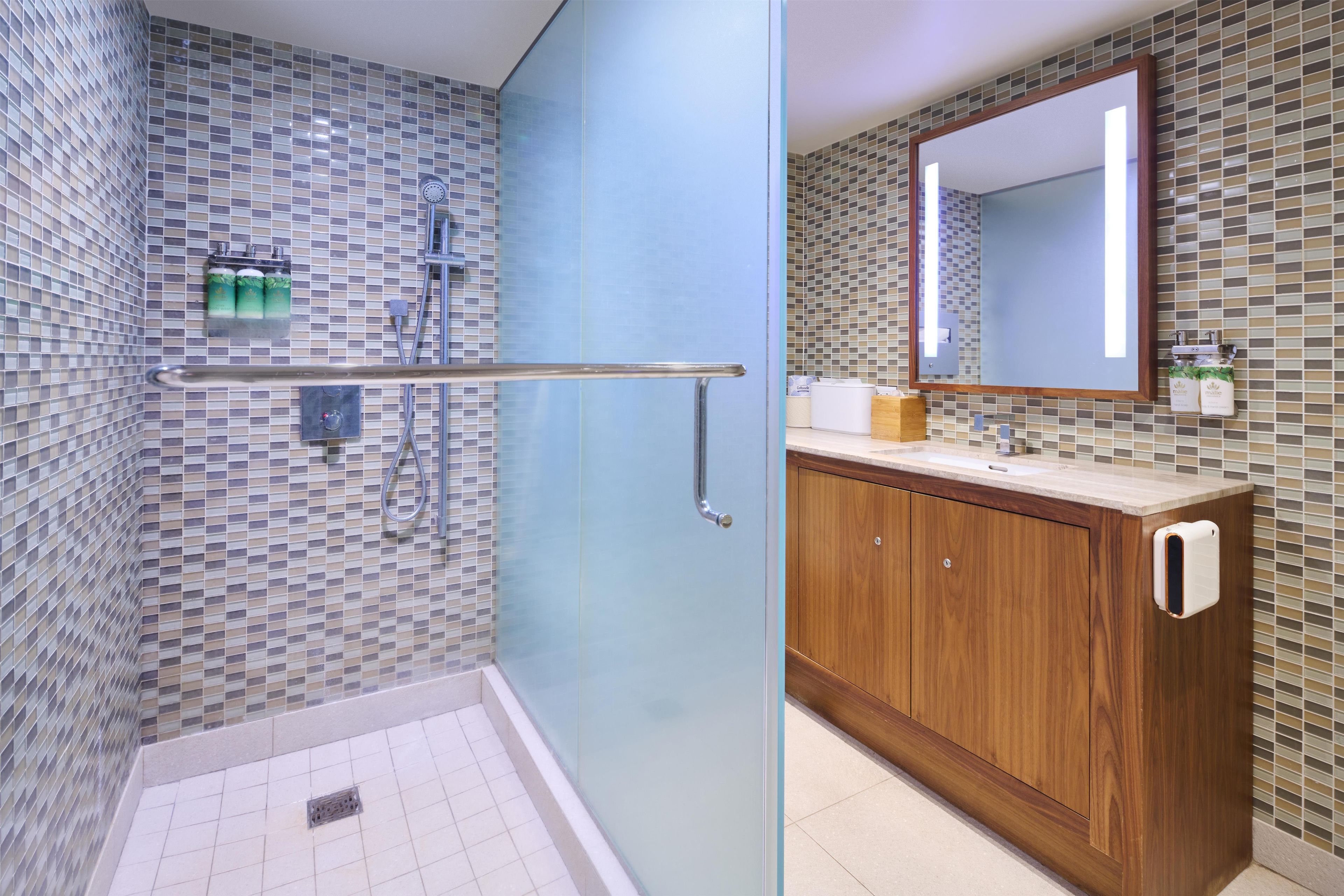 A bathroom with a glass shower enclosure, a wooden vanity, and a tiled backsplash.
