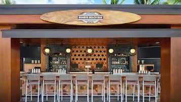 Un bar con un letrero de madera, varios taburetes y una pared con diseño.