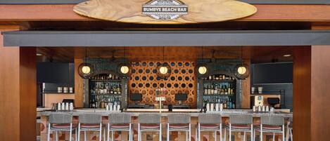 A bar with a wooden sign, multiple bar stools, and a patterned wall.