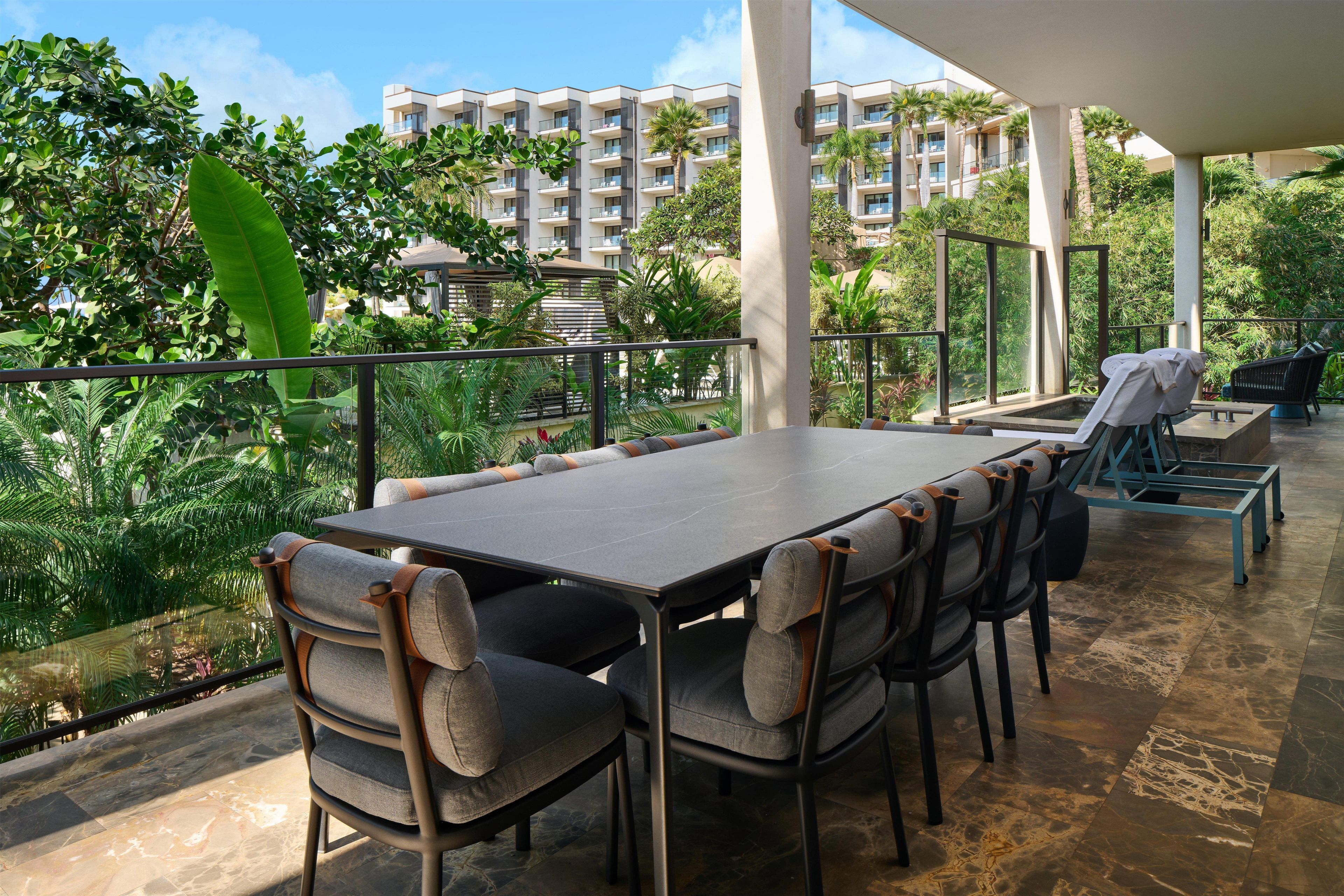 Un patio al aire libre con una mesa y sillas, rodeado de abundante vegetación y vistas a un edificio de varios pisos.