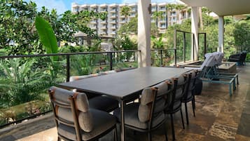 Un patio al aire libre con una mesa y sillas, rodeado de abundante vegetación y vistas a un edificio de varios pisos.