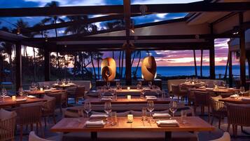 An outdoor dining area with tables set for a meal, overlooking the ocean.
