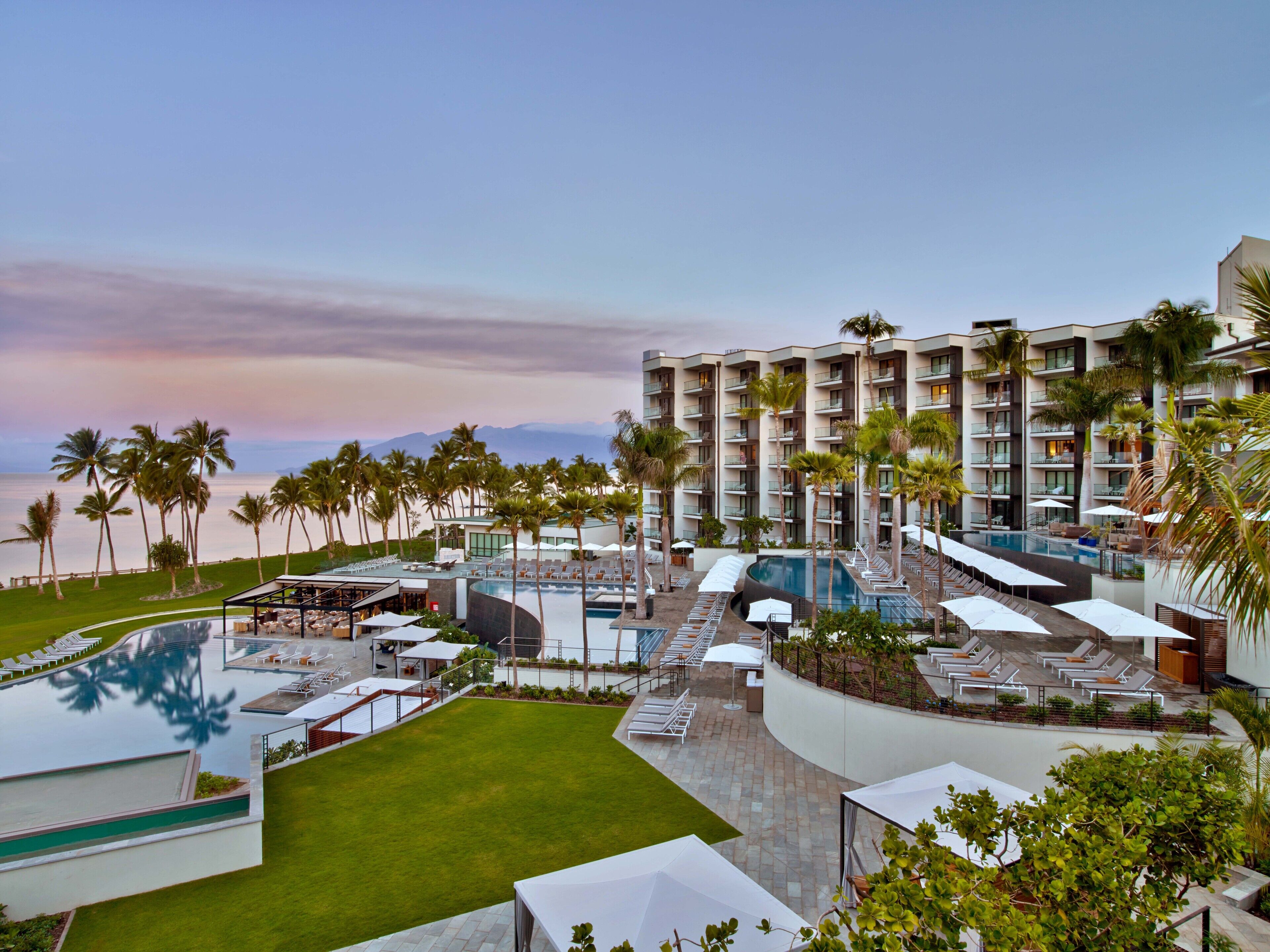 A resort with multiple swimming pools, palm trees, and a view of the ocean.