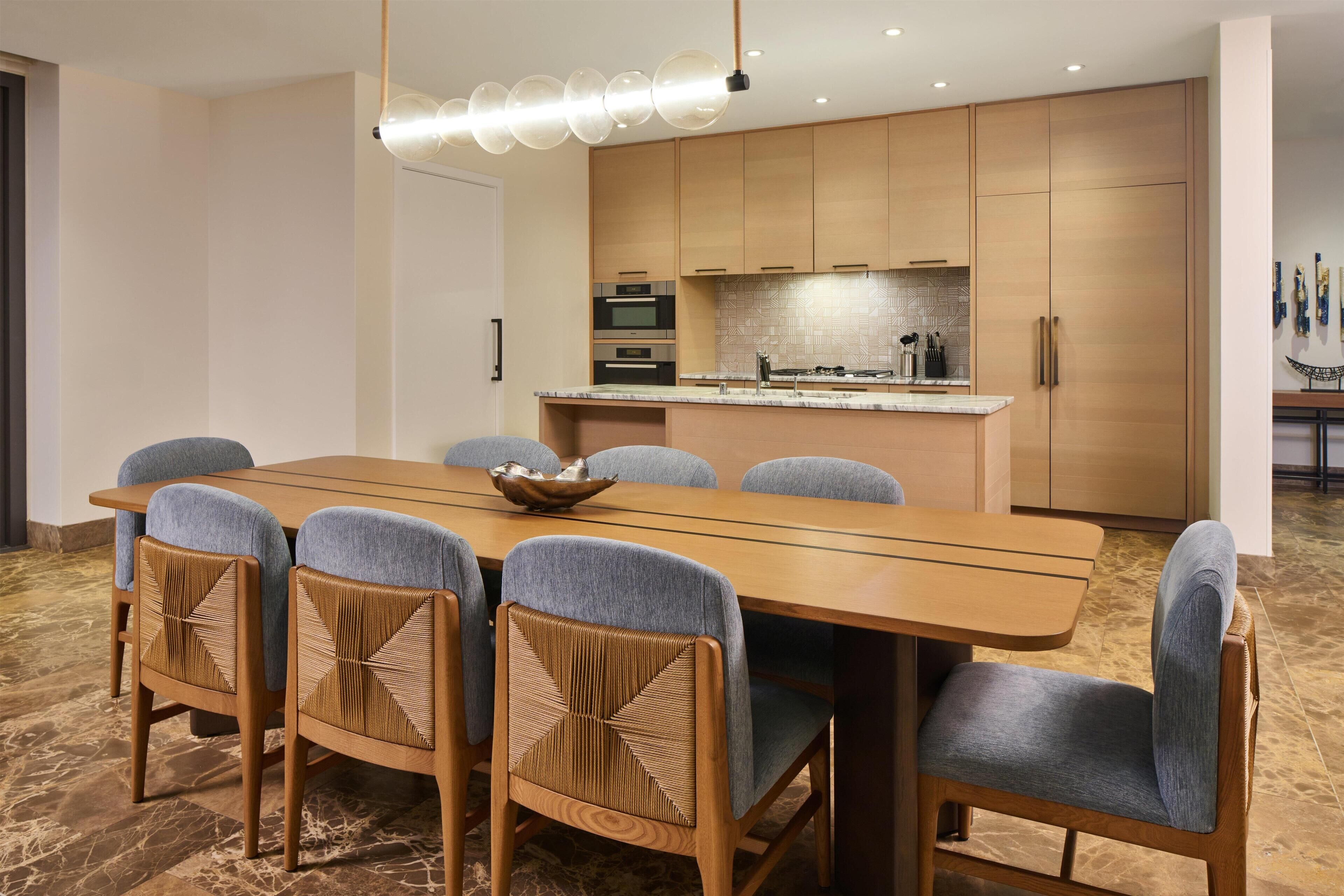 A modern kitchen with wooden cabinets, a central island, and a dining area with a long table and six chairs.