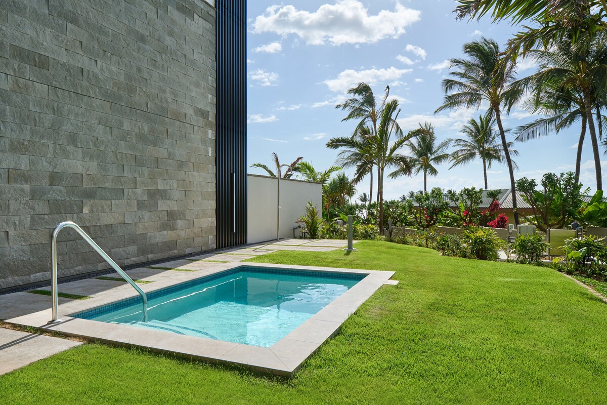 A swimming pool with a metal ladder, surrounded by a well-maintained lawn and palm trees.