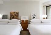 A hotel room with two beds, a nightstand, and artwork on the wall.