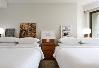 A hotel room with two beds, a nightstand, and artwork on the wall.