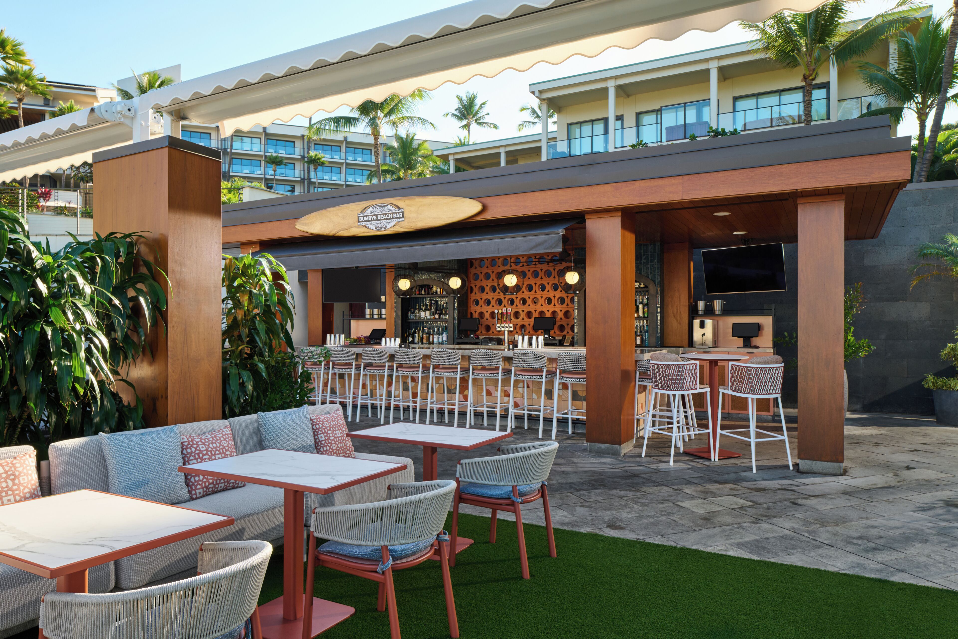 Un área de bar al aire libre con asientos, una piscina y vistas de los edificios del hotel.