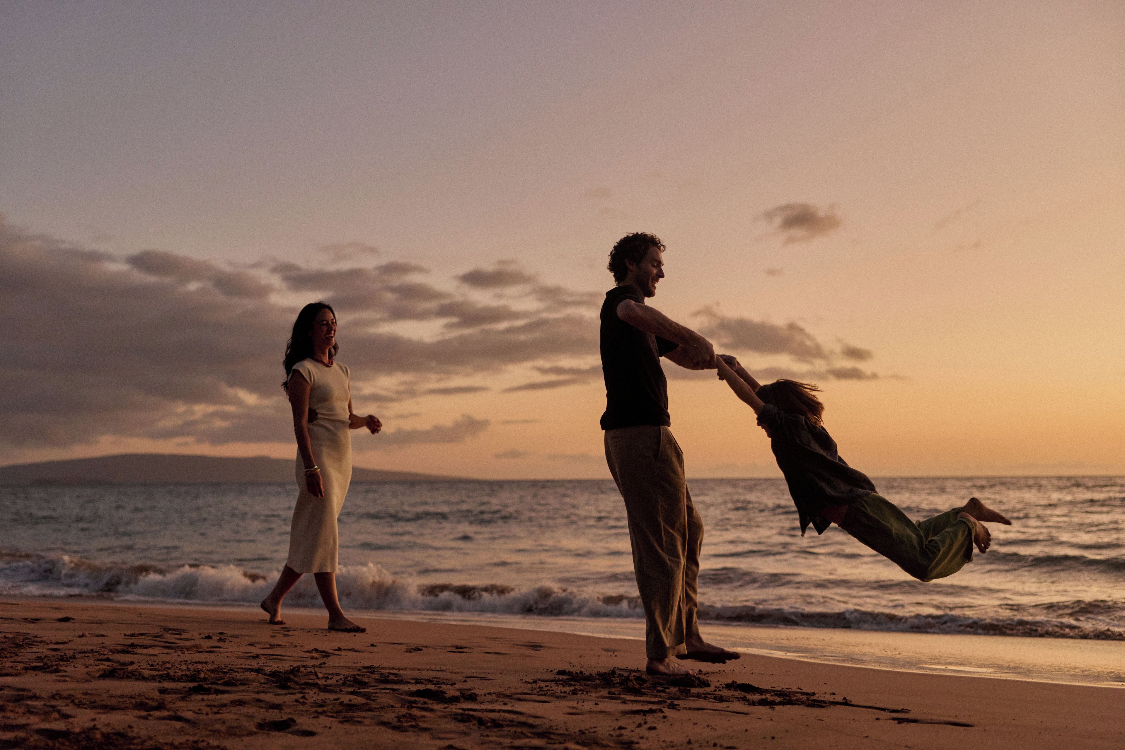 A beach scene with two people, one holding a child, and the ocean in the background.