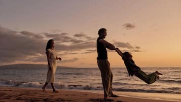 A beach scene with two people, one holding a child, and the ocean in the background.