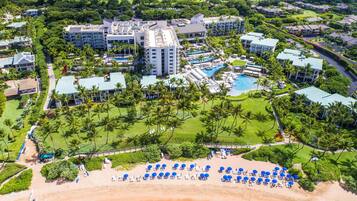 Vista aérea de un resort con varias edificaciones, un área de piscina central y una playa con tumbonas.