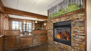 A modern kitchen with a stone fireplace, wooden cabinetry, and a large window. - Days Inn & Suites by Wyndham Gunnison (Gunnison)