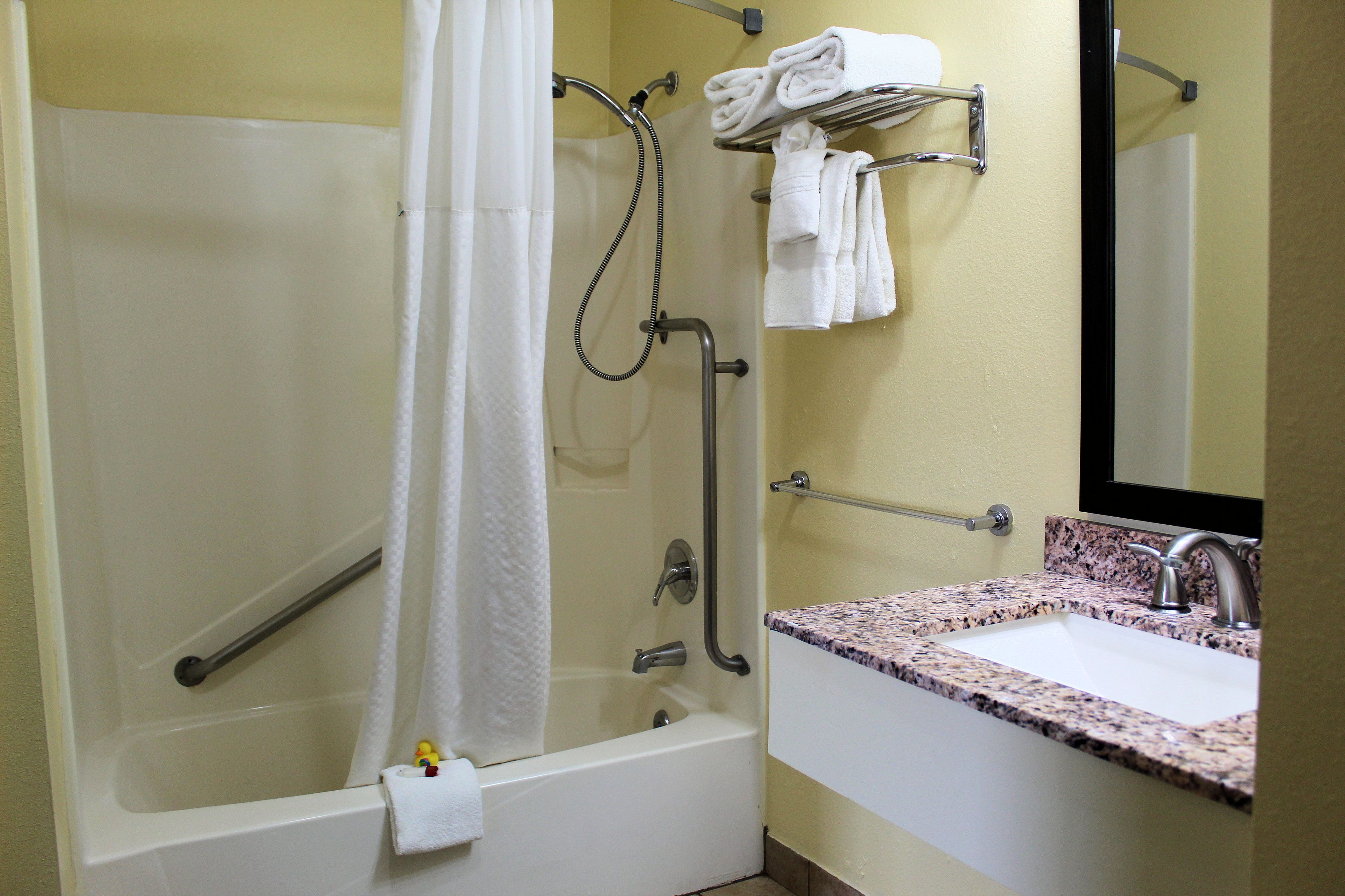 A bathroom with a shower, grab bars, a sink, and a towel rack.