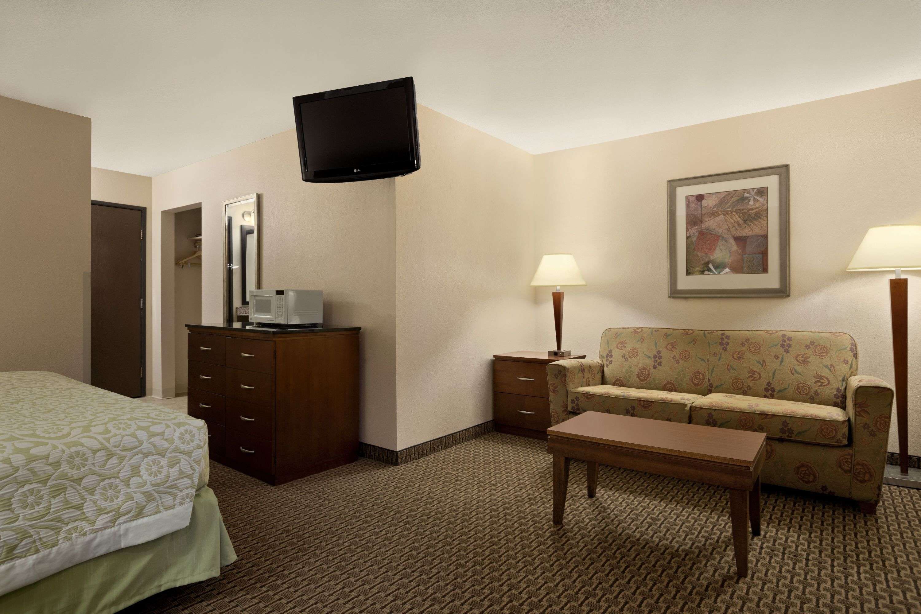 A hotel room with a bed, a dresser, a television, a sofa, a coffee table, and two lamps.