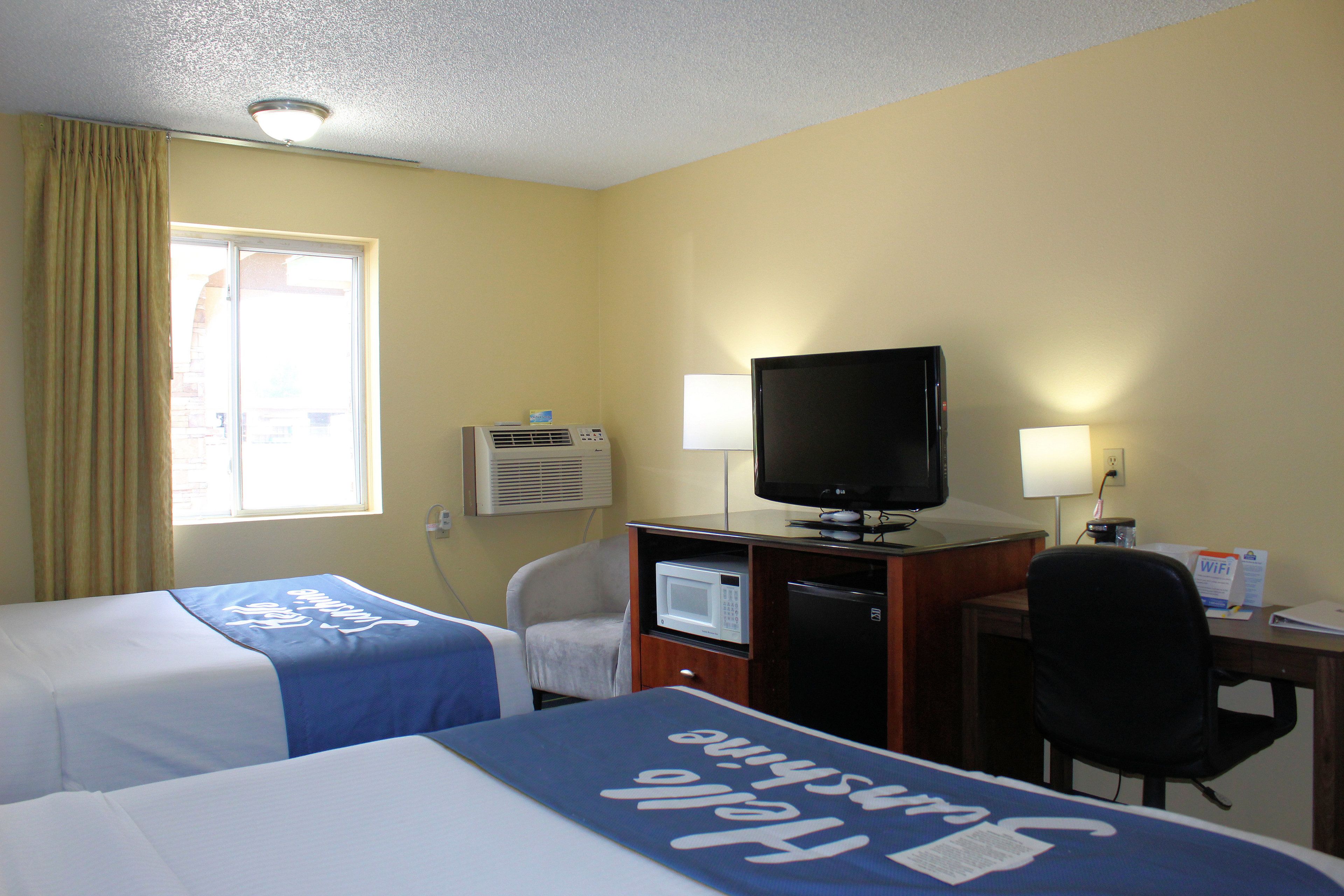 A hotel room with two beds, a desk with a television, a microwave, and a chair.