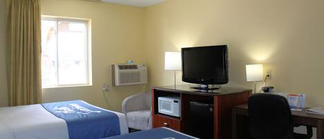 A hotel room with two beds, a desk with a television, a microwave, and a chair.