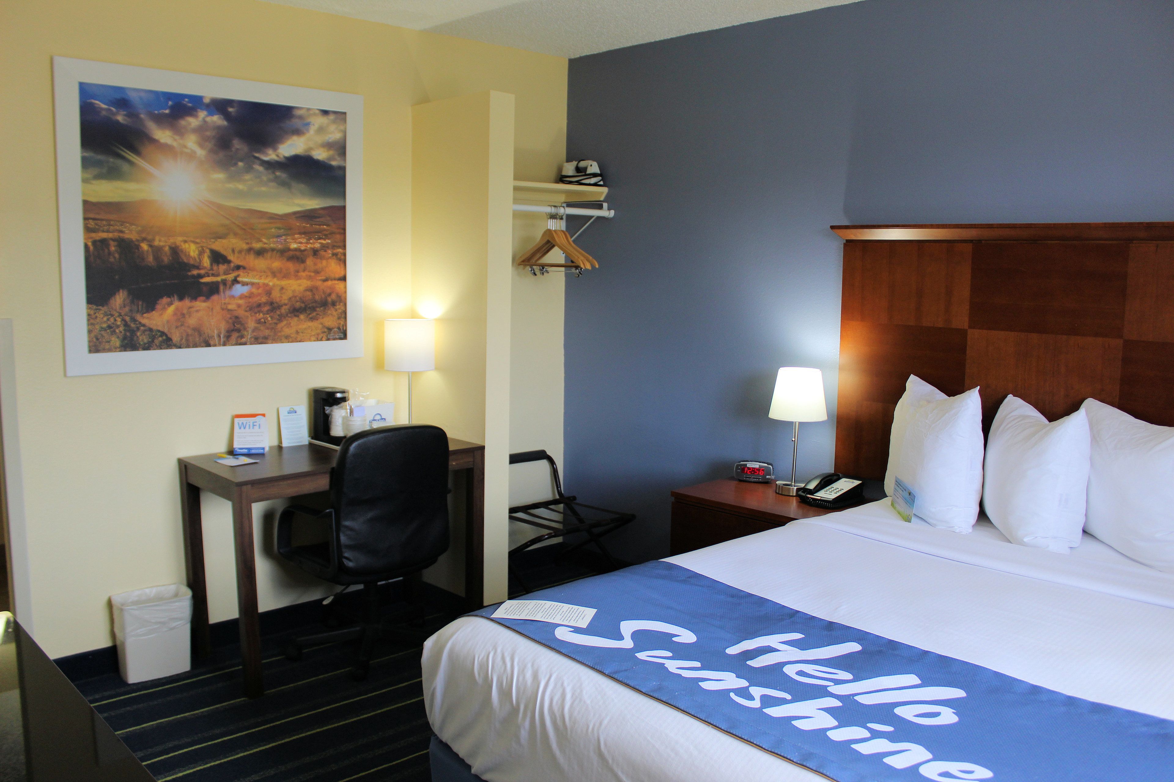 A hotel room with a bed, desk, chair, and a painting on the wall.