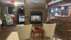 A lobby with a fireplace, two chairs, a table, a magazine rack, and a reception desk. - Days Inn & Suites by Wyndham Gunnison (Gunnison)