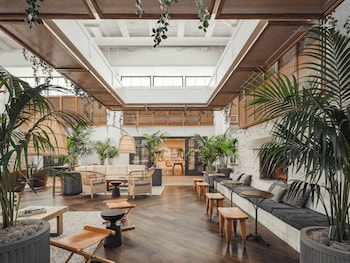 A cozy lounge area with sofas, wooden tables, and wicker ottomans, surrounded by lush greenery and a bar with shelves of bottles. at The Scott Resort & Spa