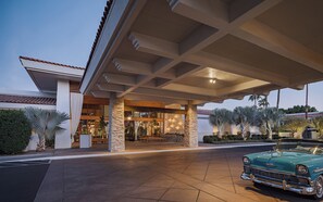 A hotel entrance with a covered patio, stone pillars, and a vintage car parked in front.