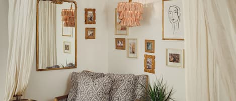 A cozy living room with a patterned sofa, a small side table, a potted plant, and a large mirror on the wall.