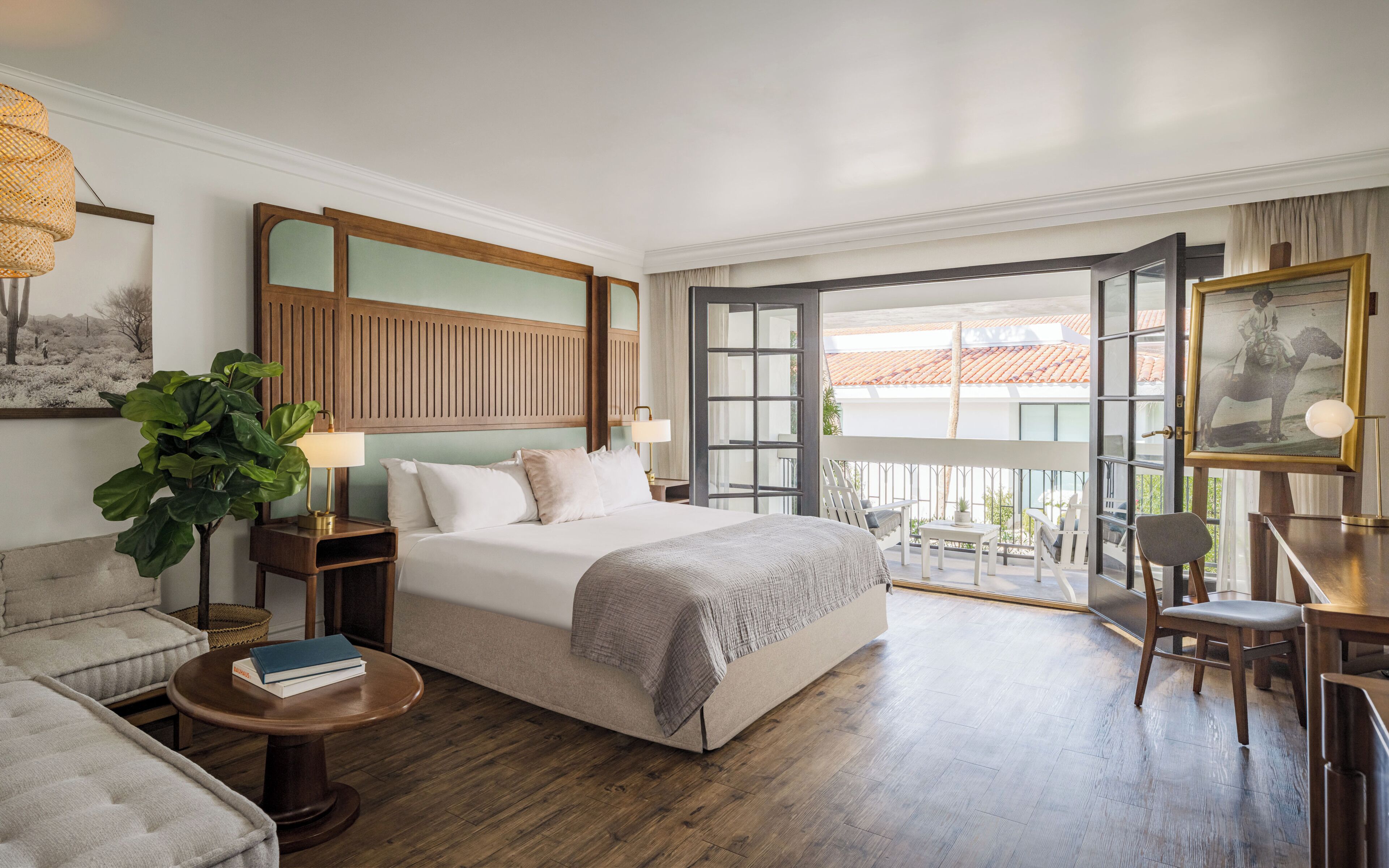 Une chambre d’hôtel comprenant un lit, des tables de chevet, un bureau, une chaise, un balcon avec vue et une grande plante.