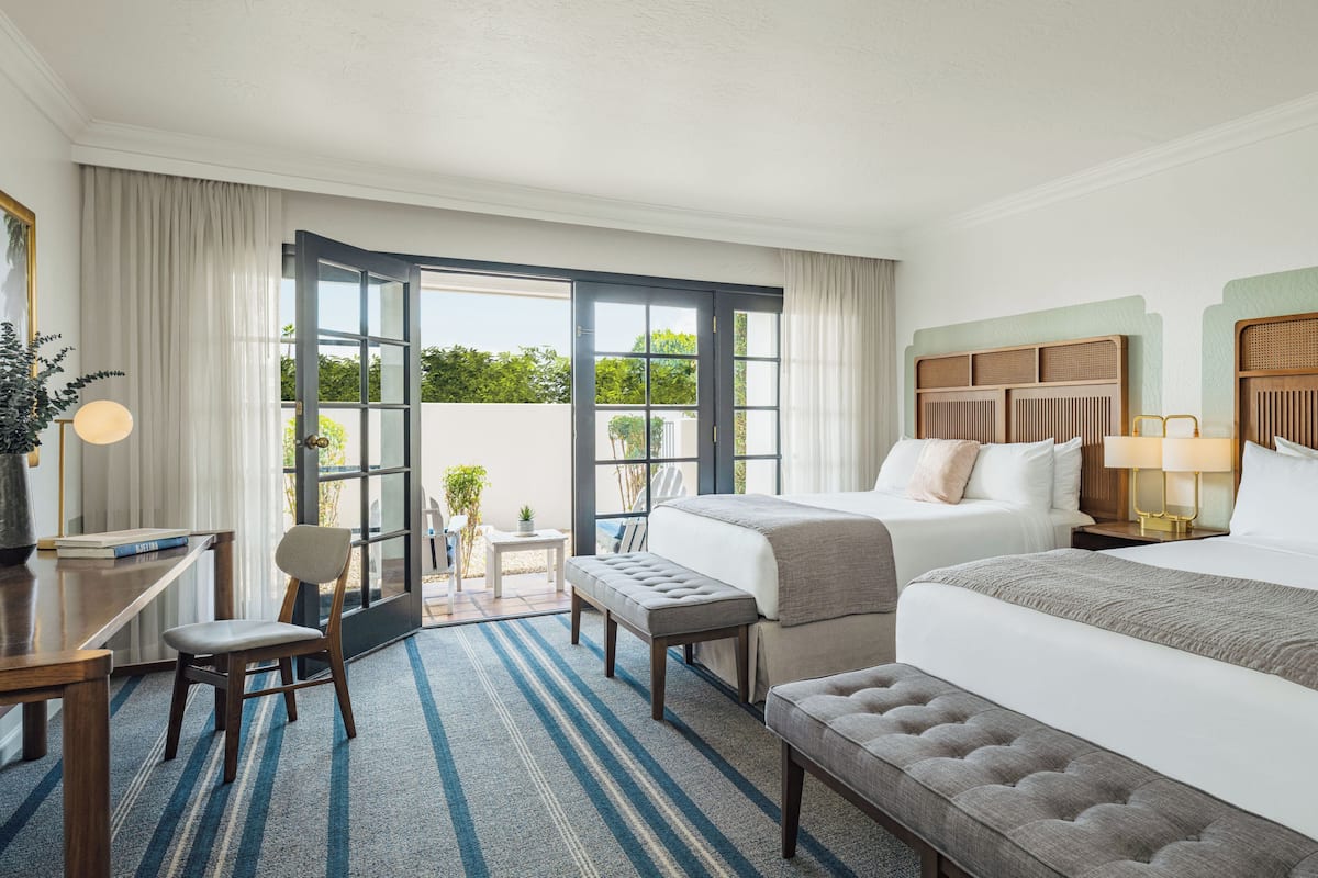 A hotel room with a bed, a desk, a chair, a bench, and a view through a glass door.