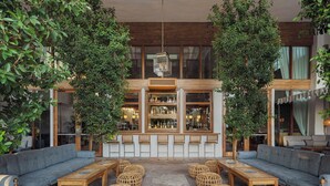 A cozy lounge area with sofas, wooden tables, and wicker ottomans, surrounded by lush greenery and a bar with shelves of bottles. - The Scott Resort & Spa  (Scottsdale)