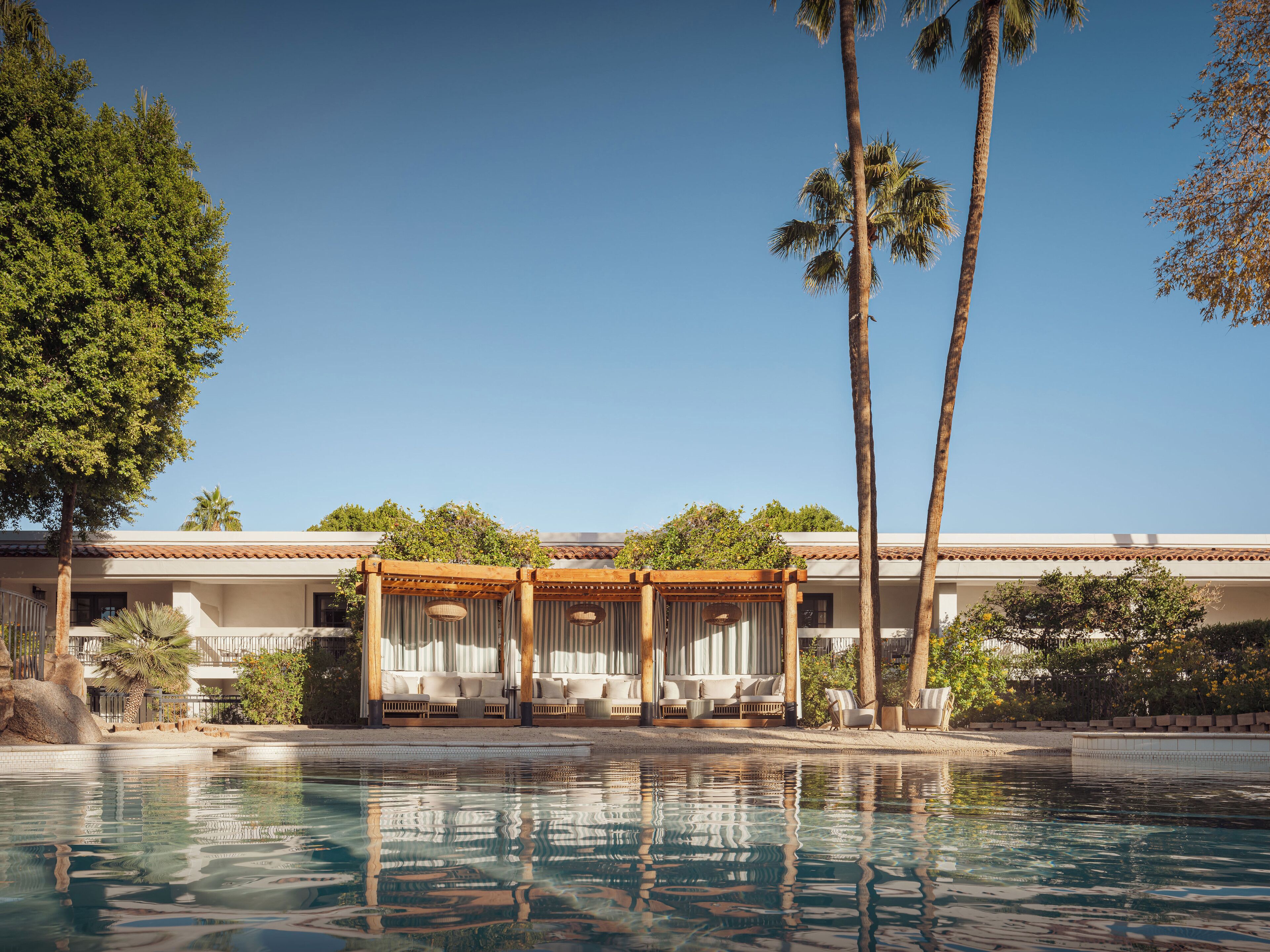 A pool area with a pergola, palm trees, and a building with a tiled roof.