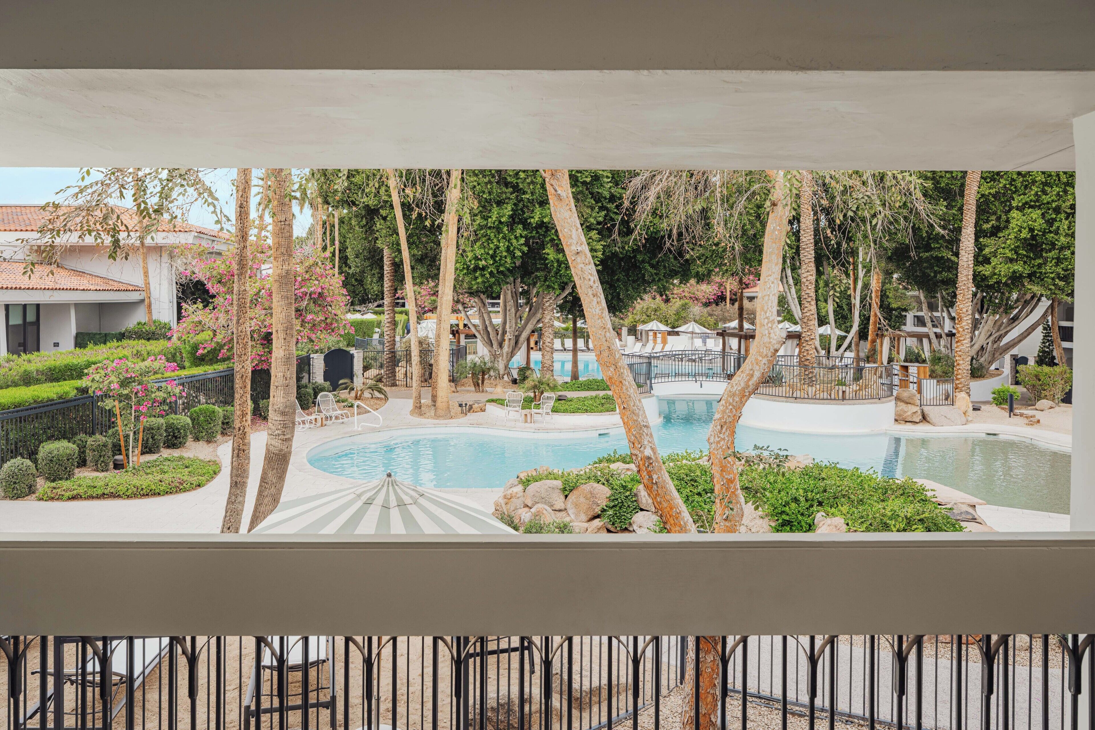 A pool area with palm trees, a lounge chair, and a building in the background.