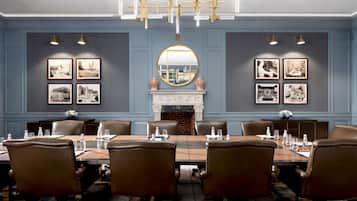 A conference room with a long table, leather chairs, framed pictures, a fireplace, and a chandelier.