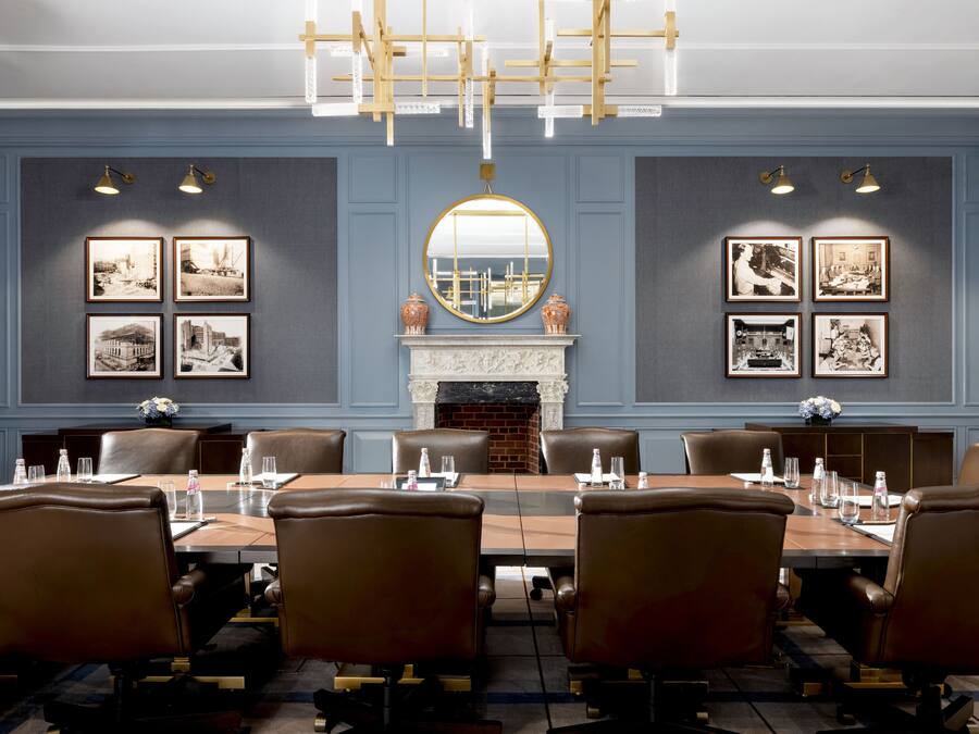 A conference room with a long table, leather chairs, framed pictures, a fireplace, and a chandelier.