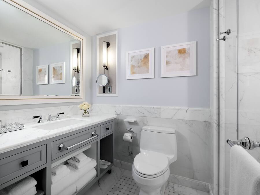 Une salle de bain moderne avec un grand miroir, un lavabo, des toilettes et une douche. Des tableaux encadrés ornent le mur, et il y a aussi un porte-serviettes.