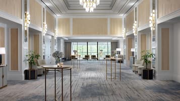 A spacious hotel lobby with a grand chandelier, multiple seating areas, and large windows offering a view of the outdoors.