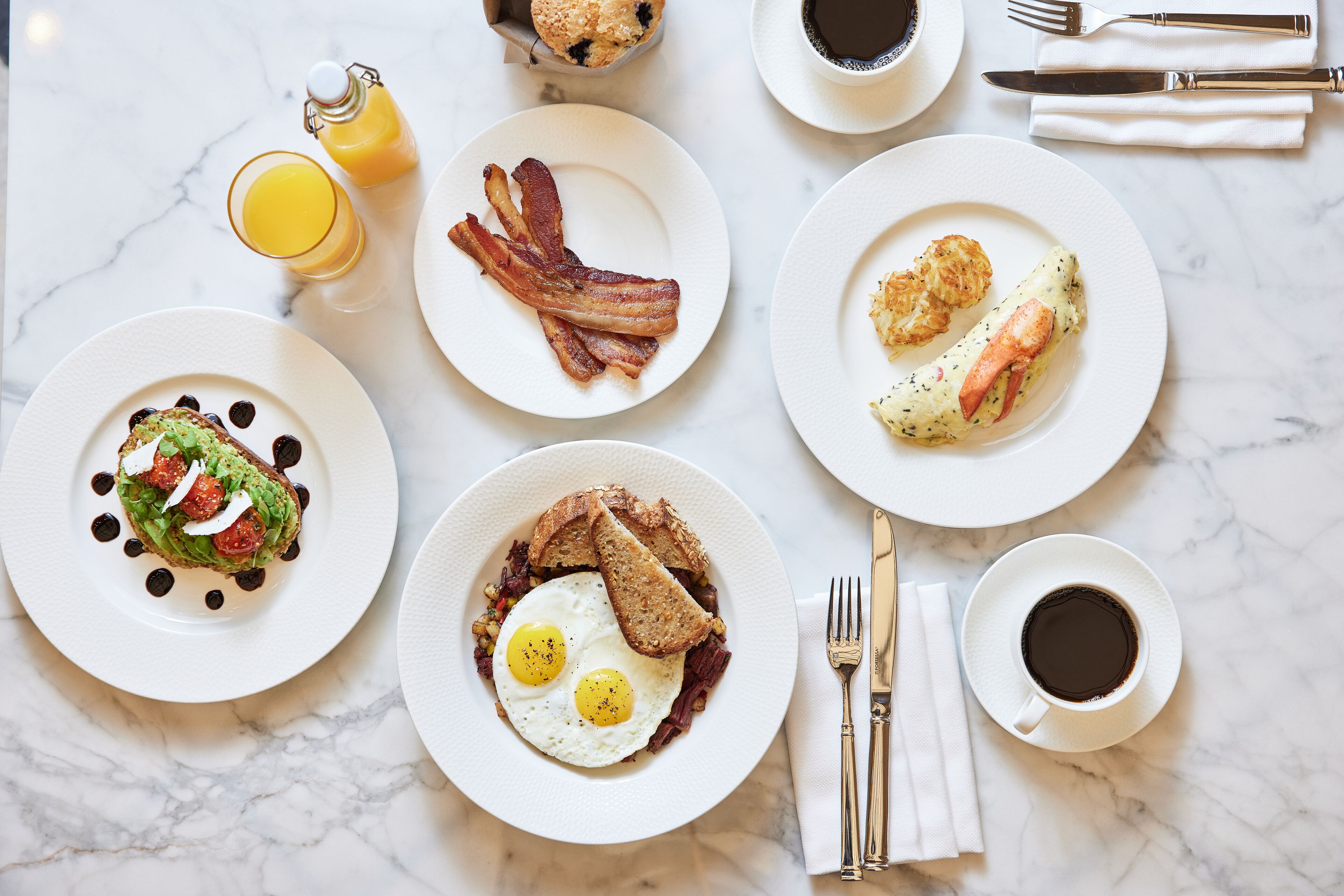 Un desayuno con varios platos, incluyendo huevos, tocino, tostadas y un muffin.