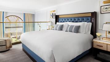 A hotel room with a large bed, a nightstand, a lamp, and a view of a building through a window.