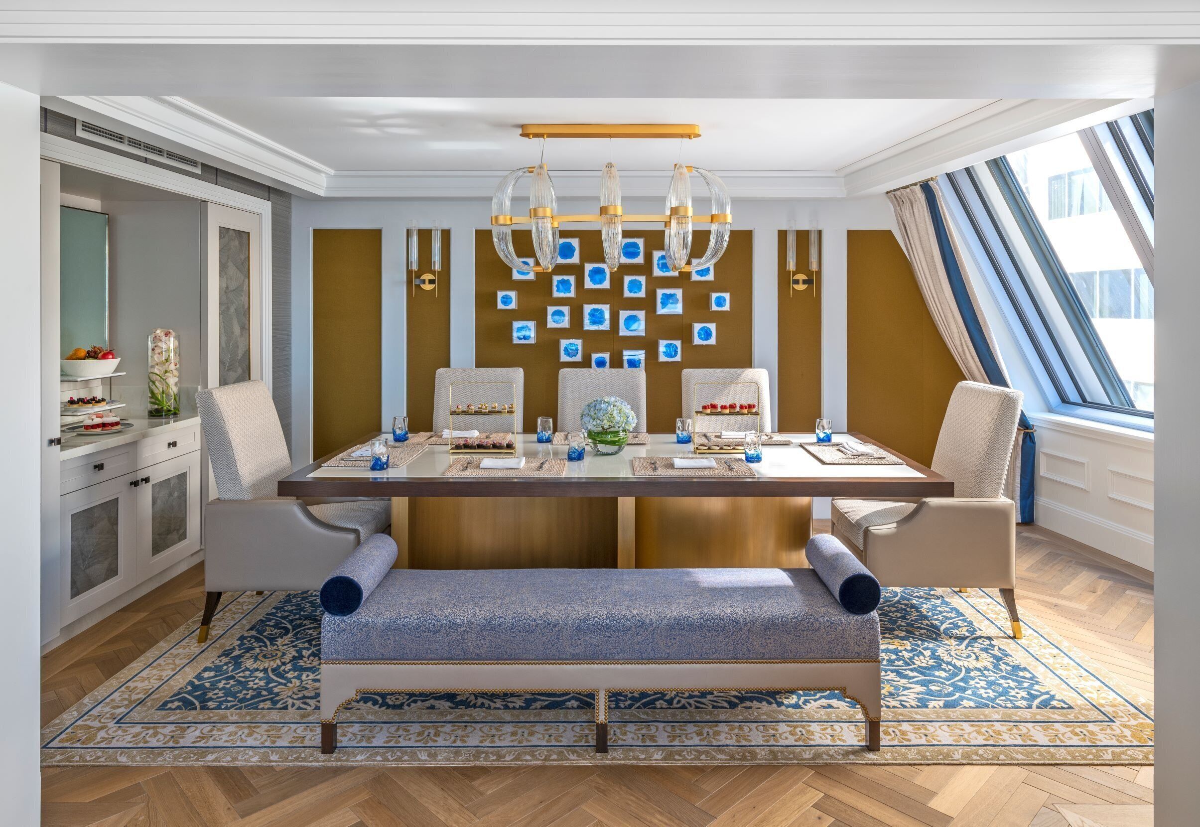 A dining area with a long table, chairs, a bench, and a chandelier.